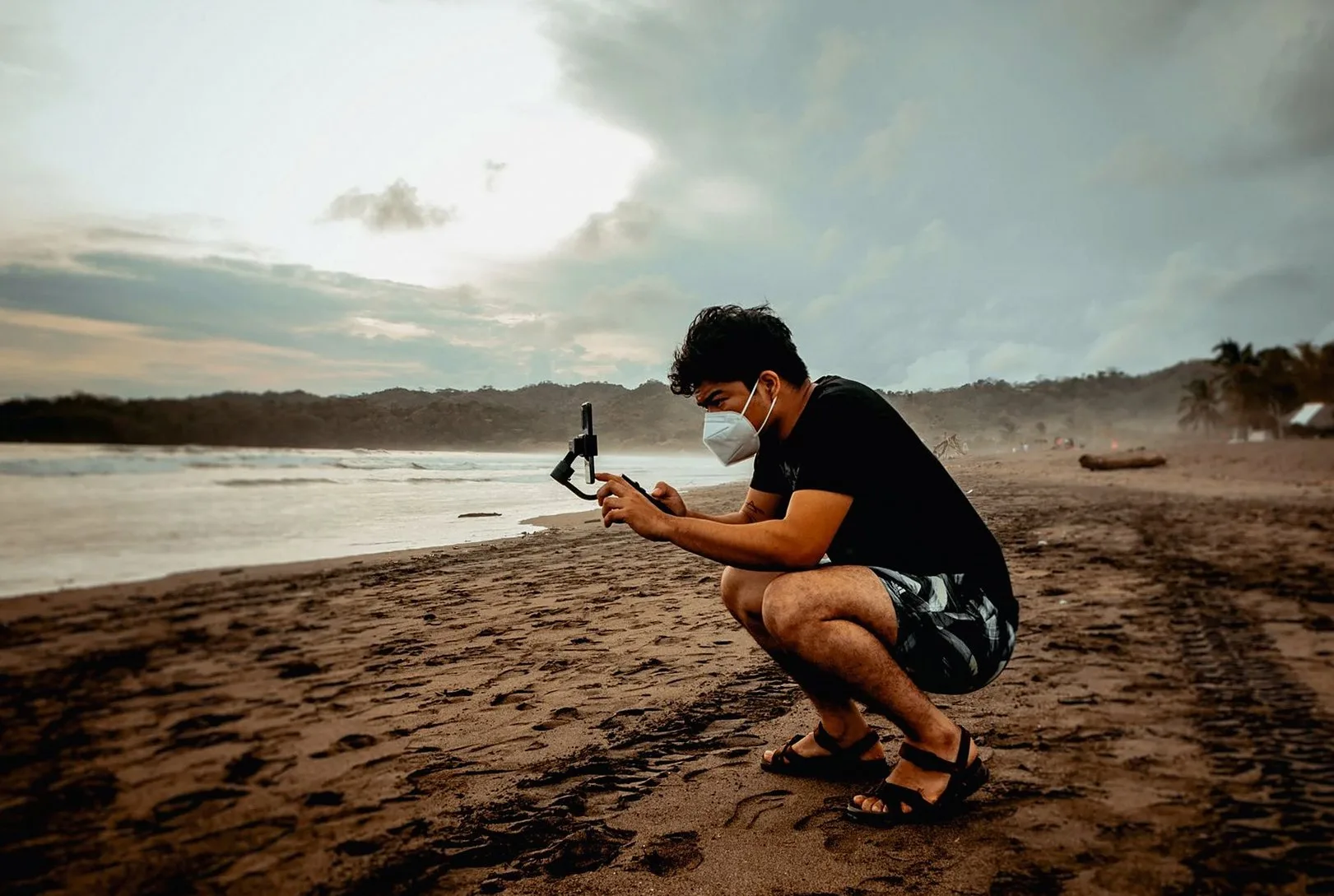 夕暮れの砂浜でスマートフォンを構えて撮影する人物